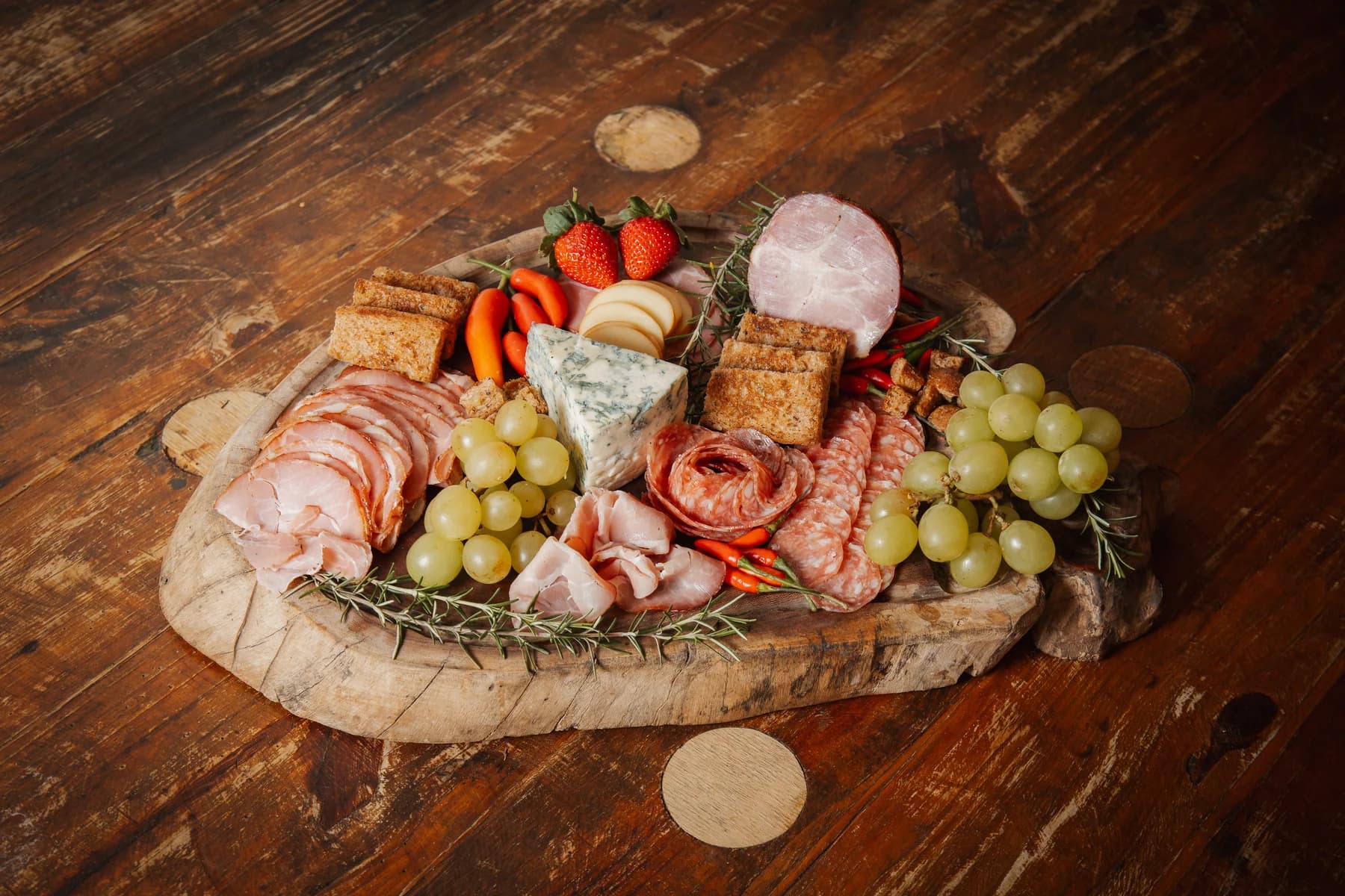 Tábua de charcutaria da Brutona com carnes, queijos e uvas sobre mesa de madeira